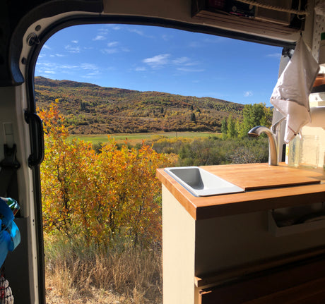 Serene RV rental view: cozy van kitchen with sink, faucet, overlooking autumn mountains & colorful foliage.