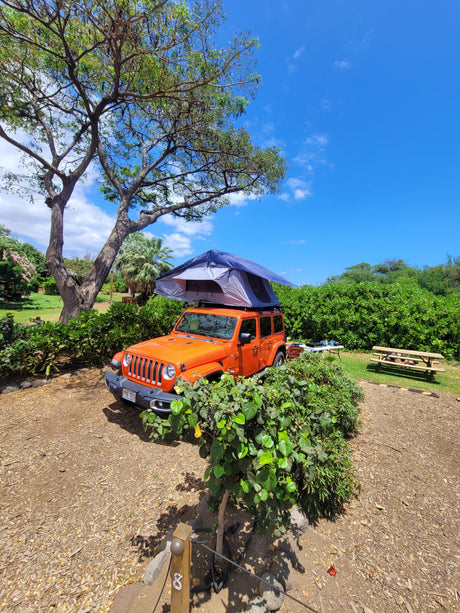 Orange Jeep with rooftop tent at sunny Hawaiian campsite. Ideal RV rental for exploring, perfect for outdoor travel.