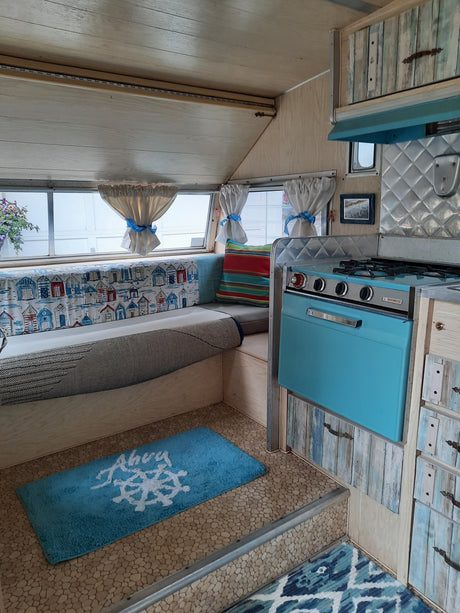 Cozy RV rental interior with light wood paneling, a turquoise stove, and nautical decor like a blue ship's wheel rug.
