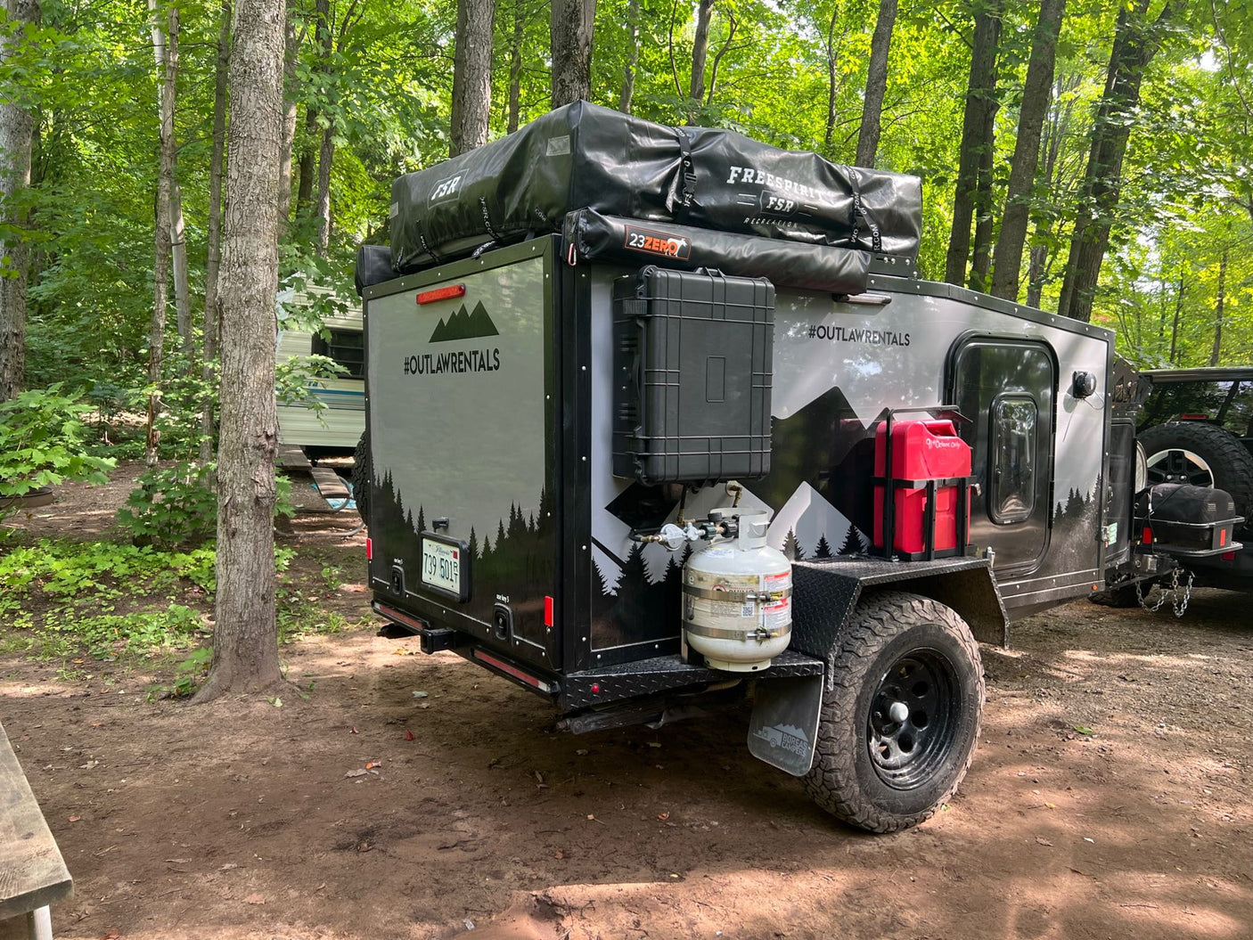 This #OutlawRentals off-road camping trailer, an RV rental, at a wooded campsite with rooftop tent.