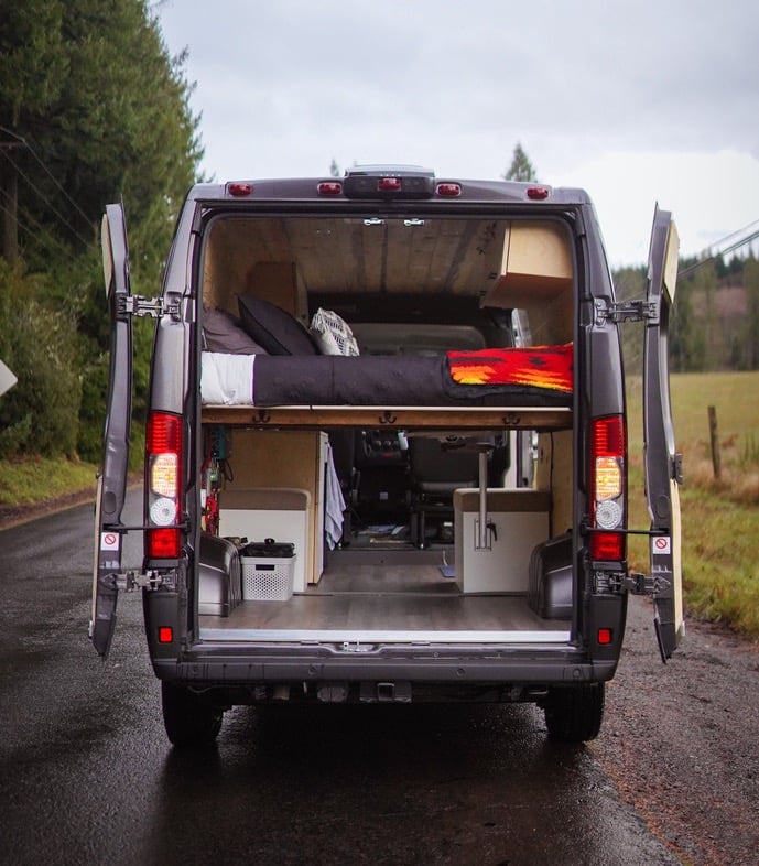  with outdoor mat and table.|Cozy RV rental interior with open back doors revealing a serene forest view. Perfect for nature lovers.|Inside a stylish RV rental: a compact kitchen with wood paneling — photo 12
