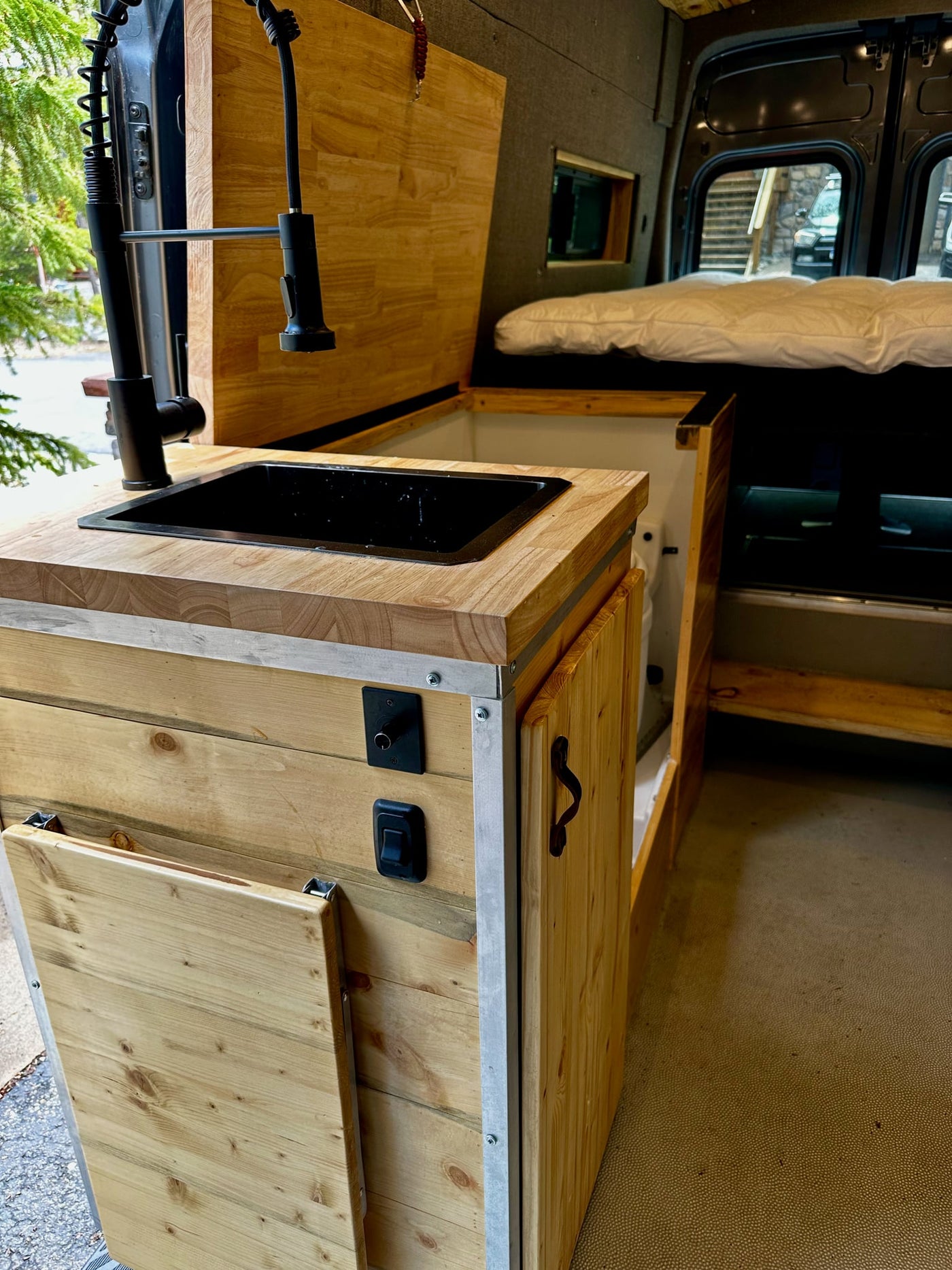  and a view outside to a house and cars.|RV rental interior: A cozy camper van features a wood ceiling — photo 12