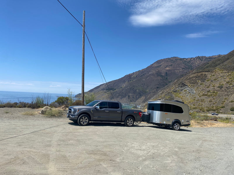 Scenic coast view with an RV rental: A pickup truck towing a sleek travel trailer on a dirt lot, mountains & ocean in the background. — photo 10