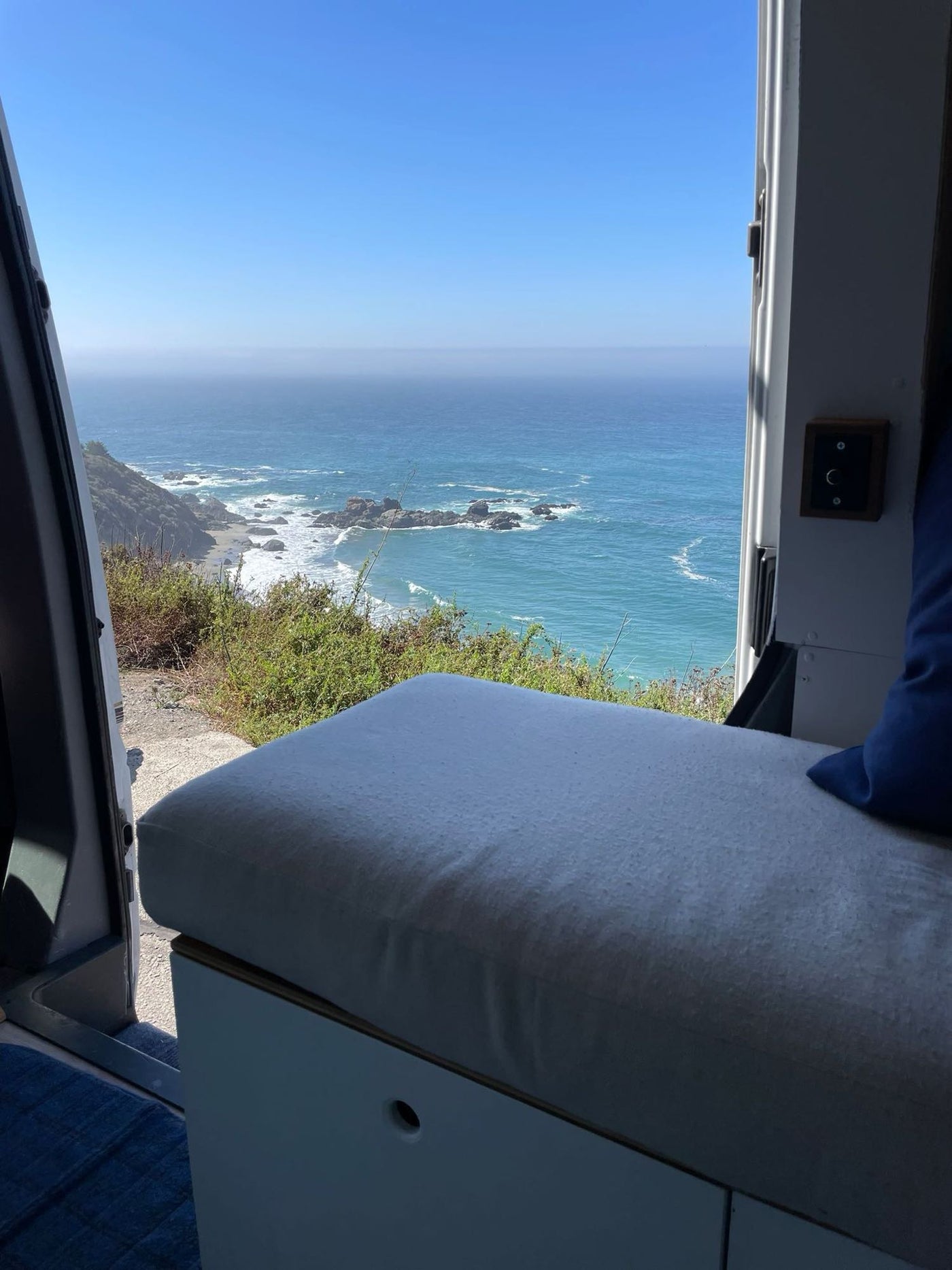  showing a rocky coast & blue sea from inside the comfortable camper.|Cozy RV rental interior featuring a bed — photo 8