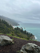 RV rental ideal for Big Sur's dramatic coast: A misty view of lush green mountains meeting turquoise ocean under an overcast sky.