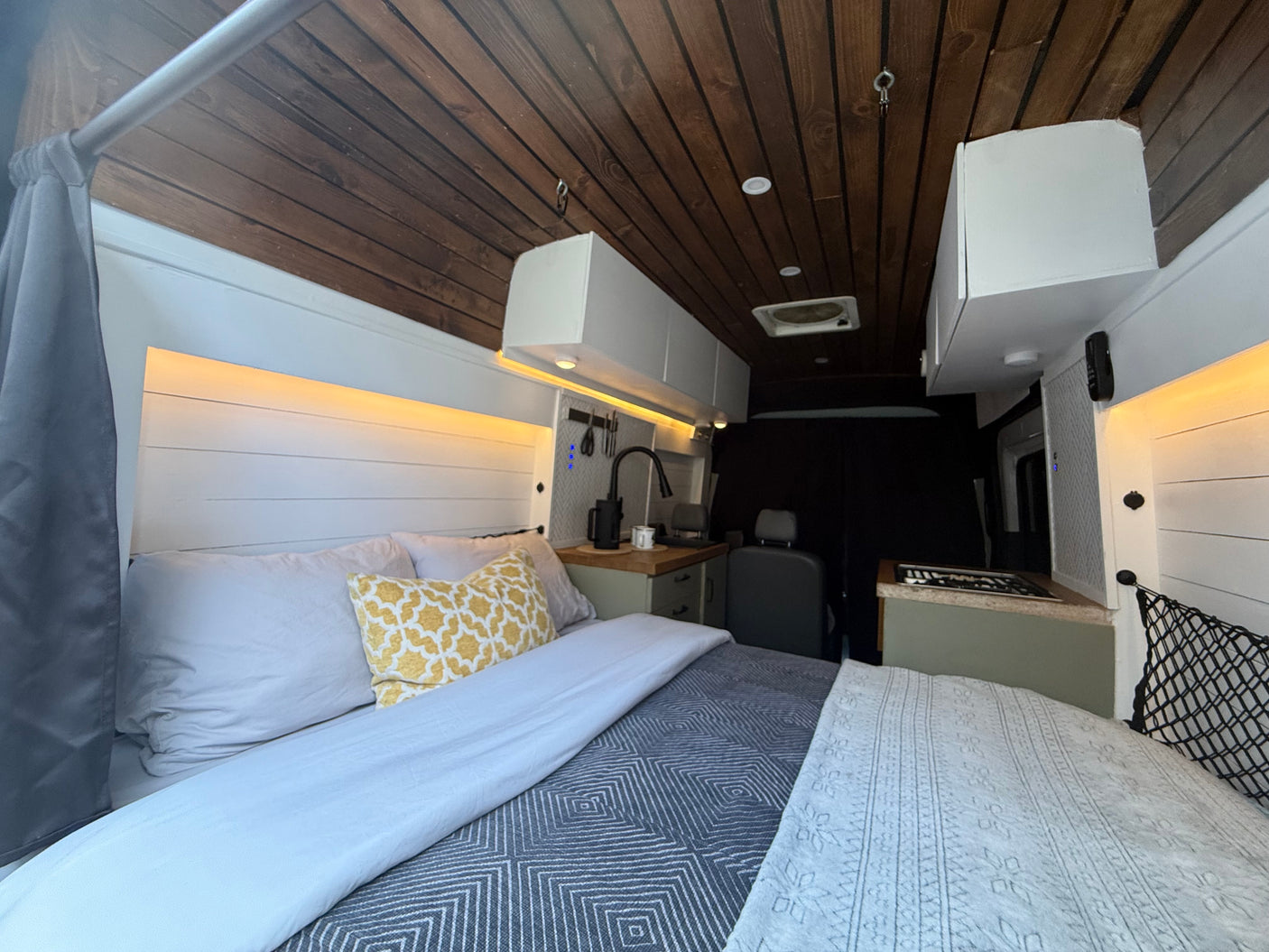 Cozy RV rental interior with a bed, shiplap walls, wooden ceiling, and a compact kitchen area for comfortable travel.