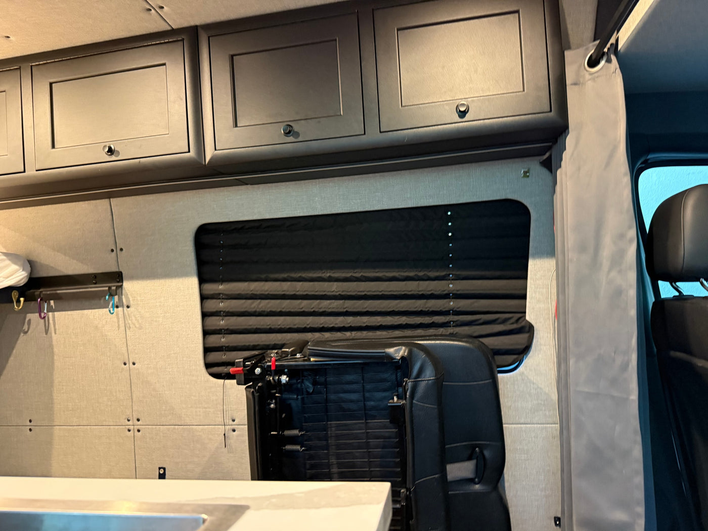 Interior of an RV rental: overhead cabinets, window with blind, and folded seat for compact living. — photo 18