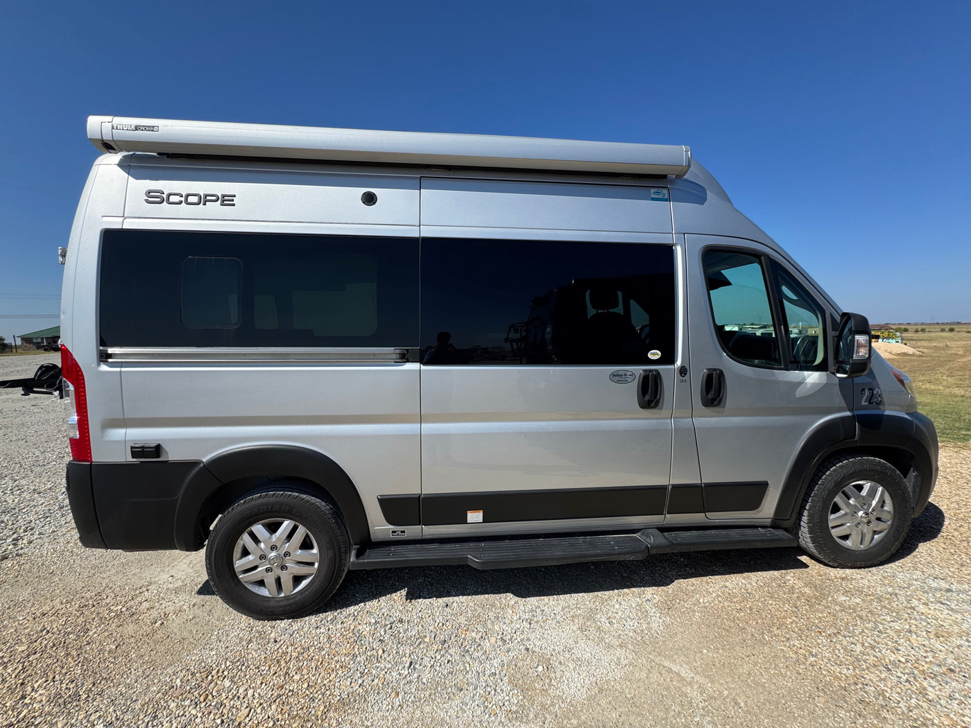 Silver Scope camper van rv rental with awning & tinted windows, parked on gravel under a clear blue sky, ready for travel. — photo 2