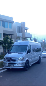 Silver Mercedes-Benz Sprinter RV rental van parked on a street, with modern residential buildings in the background.