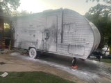 An RV rental covered in white soap suds during a wash on a driveway. Routine cleaning for adventurers.