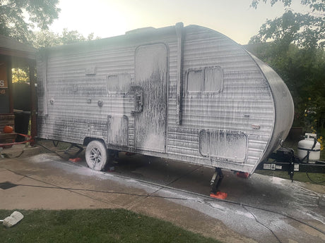 An RV rental covered in white soap suds during a wash on a driveway. Routine cleaning for adventurers.