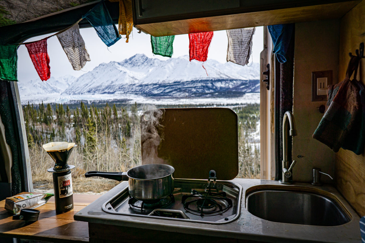 RV rental kitchen with boiling water & coffee brewing, framed by prayer flags and majestic snowy mountains. — photo 3