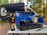 RV rental camping: cooking on a portable stove with a New Glarus beer beside the van in the woods.