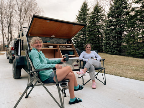 Two women relax by their RV rental, a teardrop camper with an outdoor kitchen. Ideal for easy outdoor living.