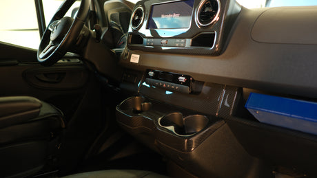 Inside a Mercedes-Benz RV rental: dashboard with steering wheel, infotainment, controls, cup holders, and carbon-look trim.