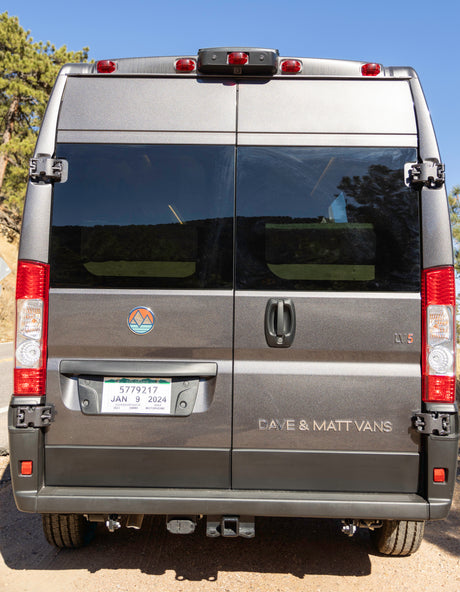 Rear view of a gray Colorado rv rental camper van, displaying its license plate, mountain logo, and "DAVE & MATT VANS" text.