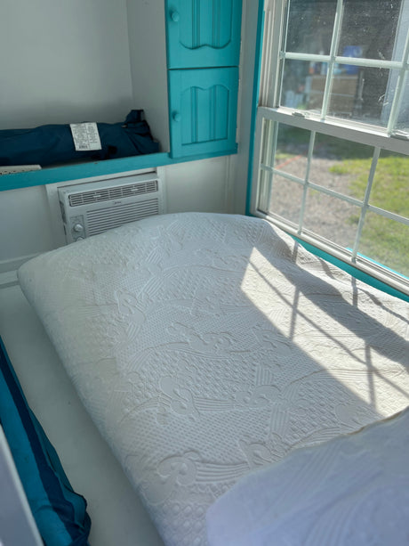RV rental: Compact interior features a comfy bed, window with sun, Midea AC unit, and turquoise cabinets.