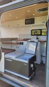 Inside a custom RV rental: modern camper van interior with a well-equipped kitchen, bed, and Dometic cooler on a slide-out.