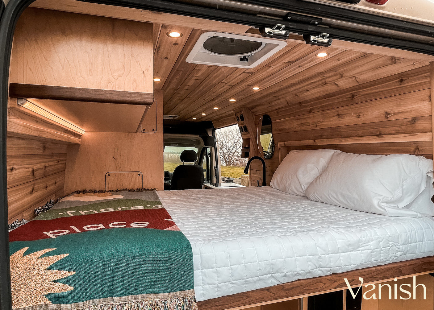 Cozy rv rental van interior with a comfy bed, warm wood paneling, LED lights, and a colorful throw blanket.
