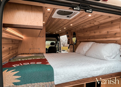 Cozy rv rental van interior with a comfy bed, warm wood paneling, LED lights, and a colorful throw blanket.