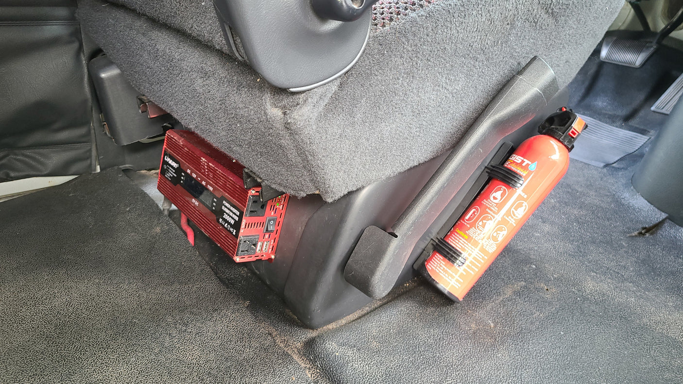 Inside an RV rental: A red power inverter mounted under the seat, next to a secured fire extinguisher.