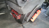 Inside an RV rental: A red power inverter mounted under the seat, next to a secured fire extinguisher.