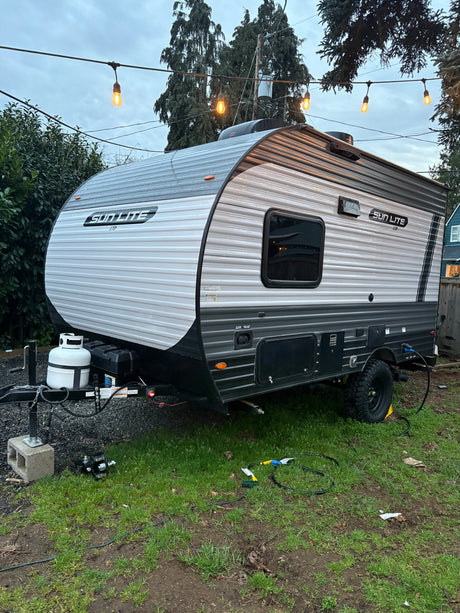 Compact Sun Lite travel trailer, perfect for your next RV rental adventure, parked under string lights in a yard.