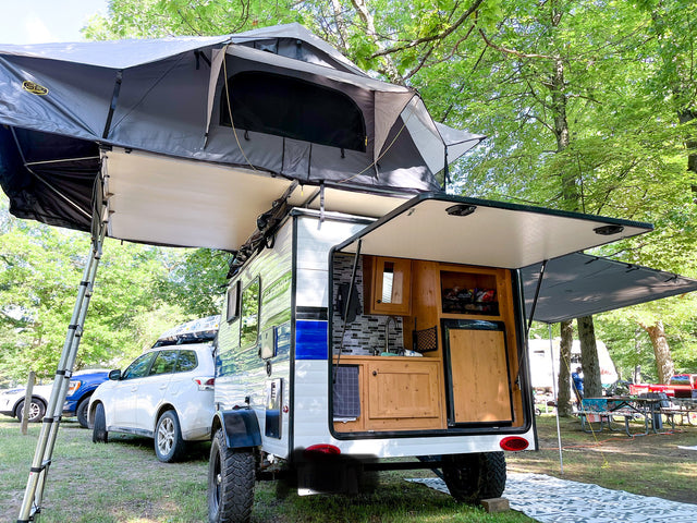 This compact rv rental with a rooftop tent and outdoor kitchen setup is ready for adventure at a lush campsite.