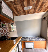 Cozy rv rental interior with a compact kitchen, bed, patterned decor, and striking wood ceiling.