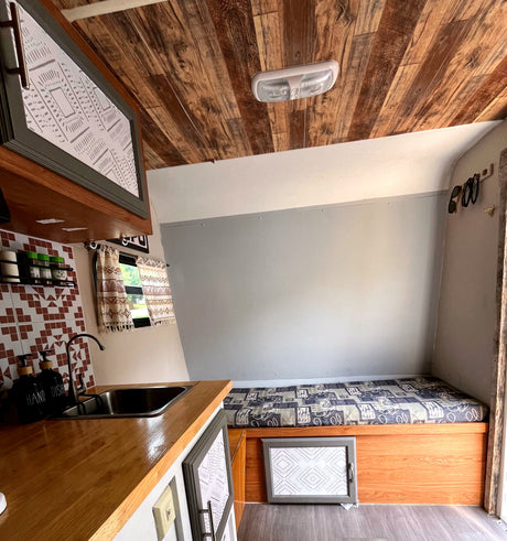 Cozy rv rental interior with a compact kitchen, bed, patterned decor, and striking wood ceiling.