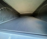 Inside a pop-top RV rental, showing the elevated sleeping platform with a light ceiling and dark fabric walls.