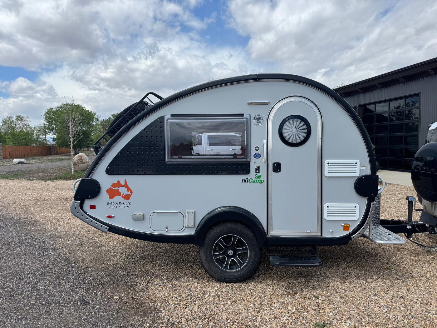 Stylish silver nuCamp T@B 320 Boondock Edition teardrop camper, an ideal RV rental for outdoor adventures, parked on gravel. — photo 2