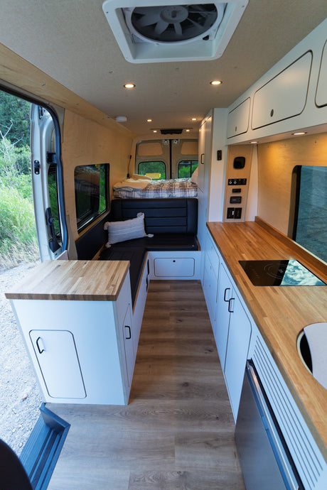 Bright, modern RV rental interior with wood accents, featuring a full kitchen, living area, and comfy bed.