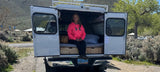 Enjoying an RV rental getaway: A woman & dog relaxing at their camper van campsite in sunny Nevada.