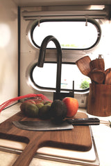Inside an RV rental kitchen: a cutting board, knife, limes, avocado, and apple. Fresh ingredients for a meal on the road.