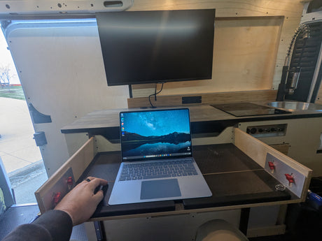 Cozy RV rental interior transformed into a compact mobile office and kitchen, featuring a laptop and monitor setup.