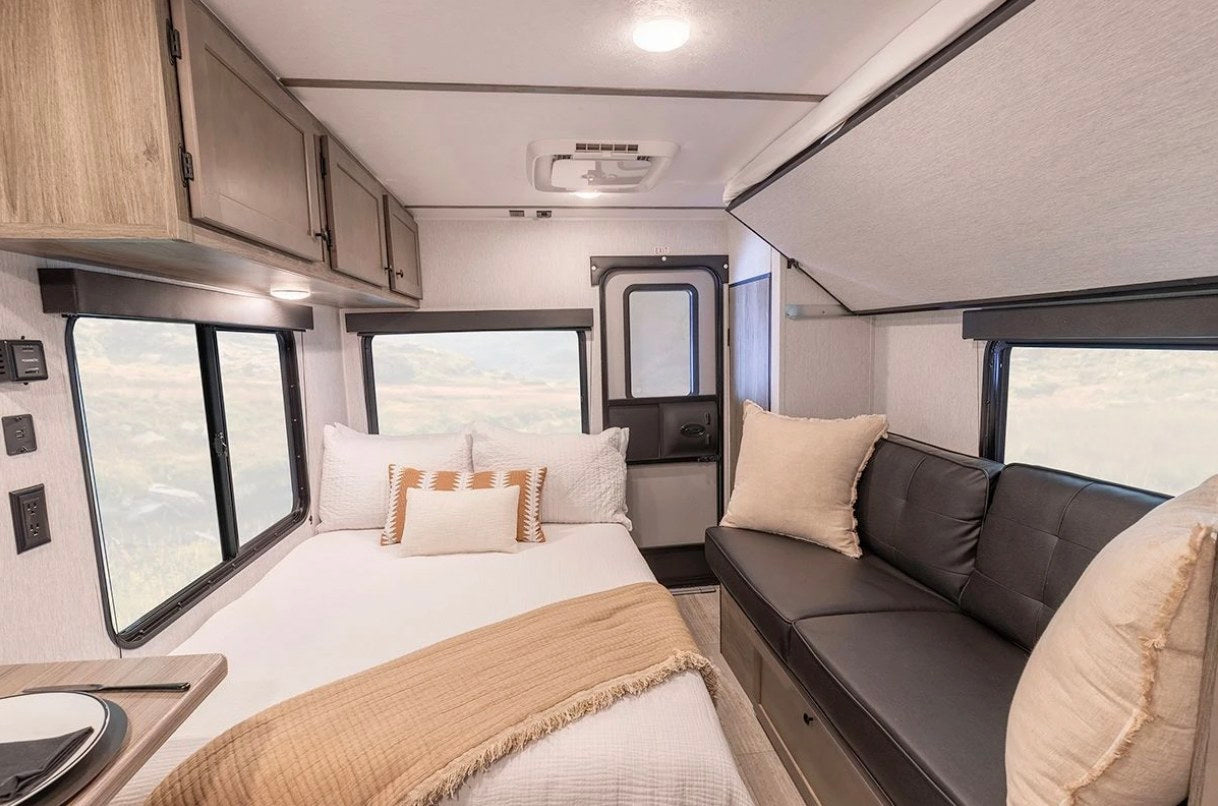 Experience comfort in this RV rental's cozy interior, featuring a full bed, lounge area, and overhead cabinets for storage.