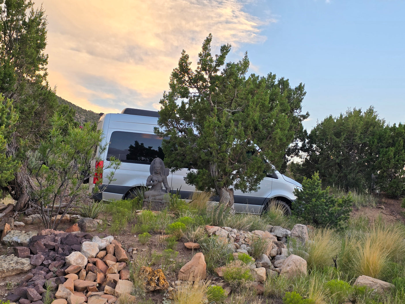 RV rental in a scenic natural setting, silver van beside a Buddha statue under a serene sky. Ideal for tranquil travel.