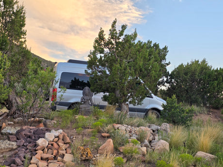 RV rental in a scenic natural setting, silver van beside a Buddha statue under a serene sky. Ideal for tranquil travel.