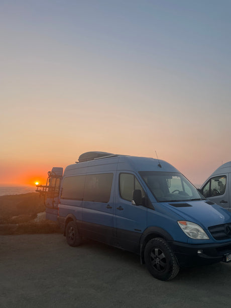 Scenic RV rental: Blue Sprinter van at sunset over the ocean, bikes on rear. Ideal for adventure.