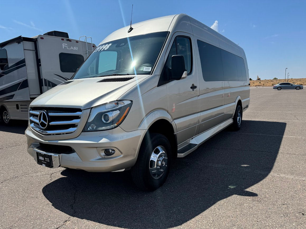 This light tan Mercedes-Benz Sprinter van, a perfect RV rental, is parked outdoors on asphalt beside a Flair RV.