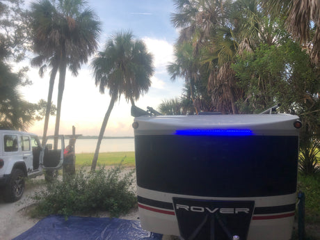 ROVER RV rental by a lake, surrounded by palm trees, a Jeep, and a person. Enjoy the outdoor adventure!