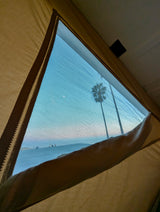 Relaxing inside an RV rental with a scenic view. A screen window frames a palm tree, crescent moon, and distant landscape under a blue sky.