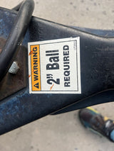 Close-up of an RV rental trailer hitch showing a "WARNING 2" Ball REQUIRED" sticker on dark metal for safe towing.
