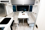 Modern rv rental interior, showcasing a bright, compact dining area with a table and bench seating, plus a small kitchen.