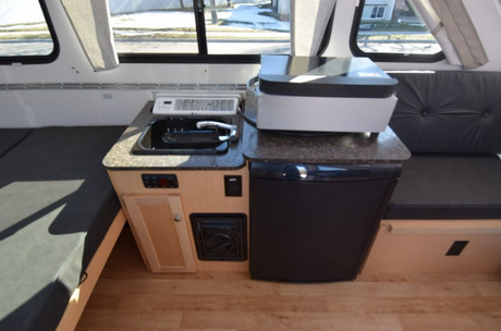 Explore a compact **RV rental** kitchen area featuring a sink, refrigerator, and comfortable bench seating.