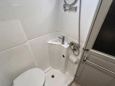 This rv rental features a compact wet bath, including a toilet, corner sink with faucet, and a handheld shower.