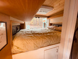 Cozy RV rental sleeping area with a comfortable bed, wood interior, and nature views from the back.