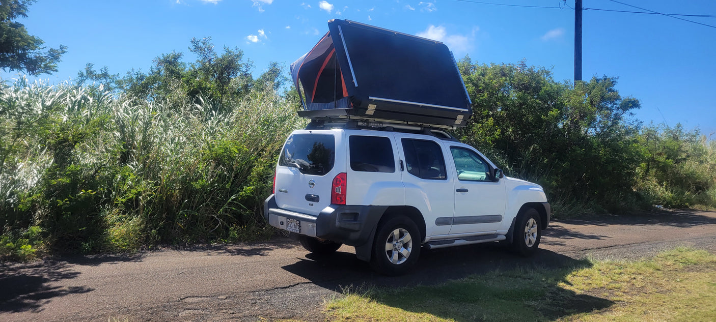 White Nissan Xterra SUV with a deployed rooftop tent, ideal for an RV rental adventure in lush greenery.