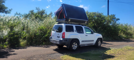 White Nissan Xterra SUV with a deployed rooftop tent, ideal for an RV rental adventure in lush greenery.